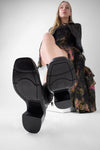 Women wearing black ankle boots with a visible brand logo on the rubber sole on a white background
