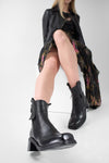 Women wearing black leather ankle boots with zips with a plain background