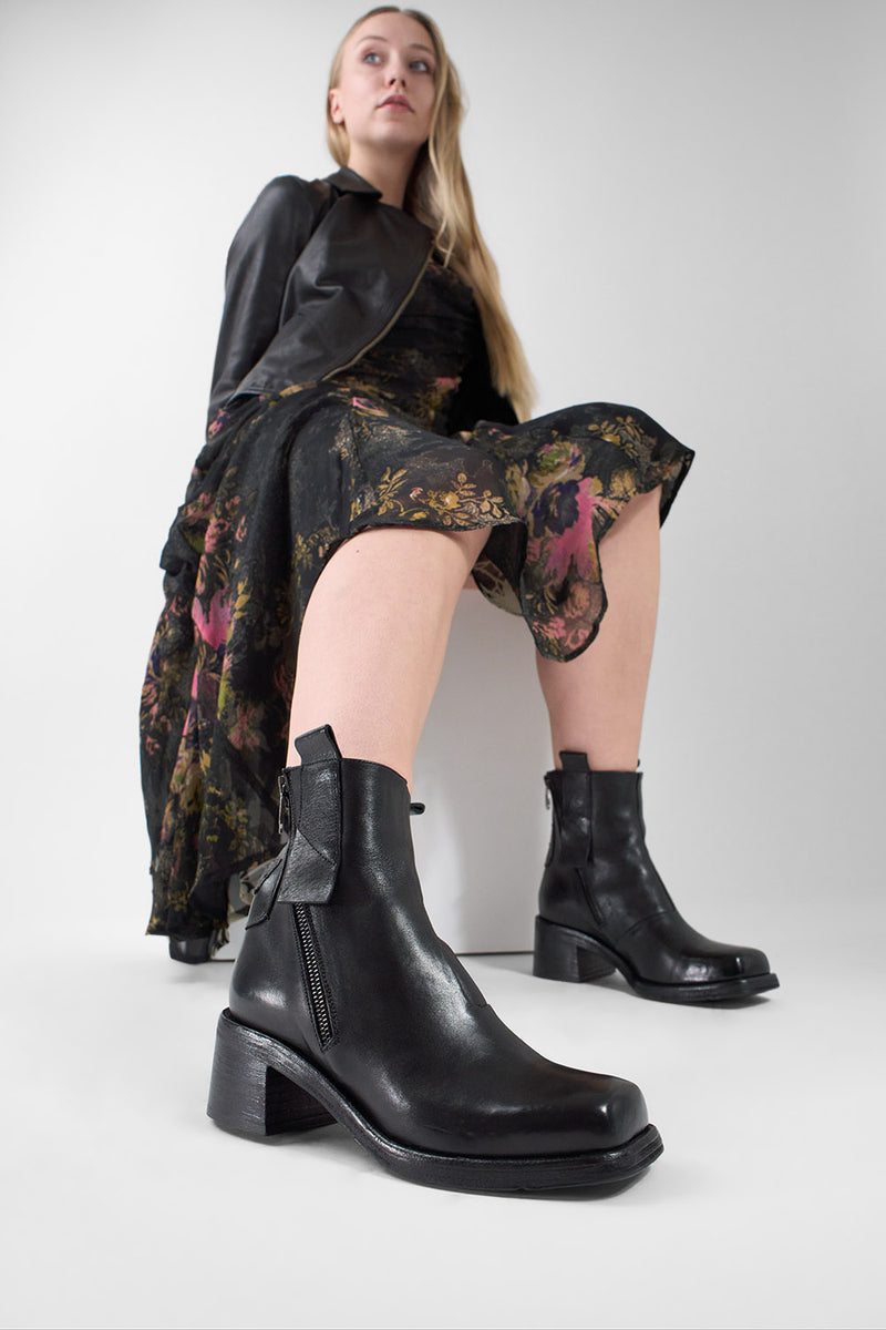 Woman wearing black leather boots, a floral dress and leather jacket on a white background
